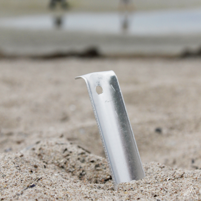 Ein silberner Sandanker steckt am Strand im Boden